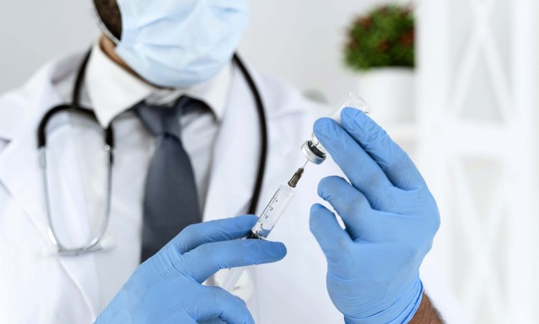 blurred doctor with medical mask holding syringe